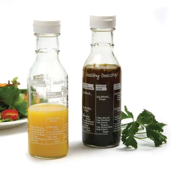 Two bottles of salad dressing with a salad in the background on a white surface.